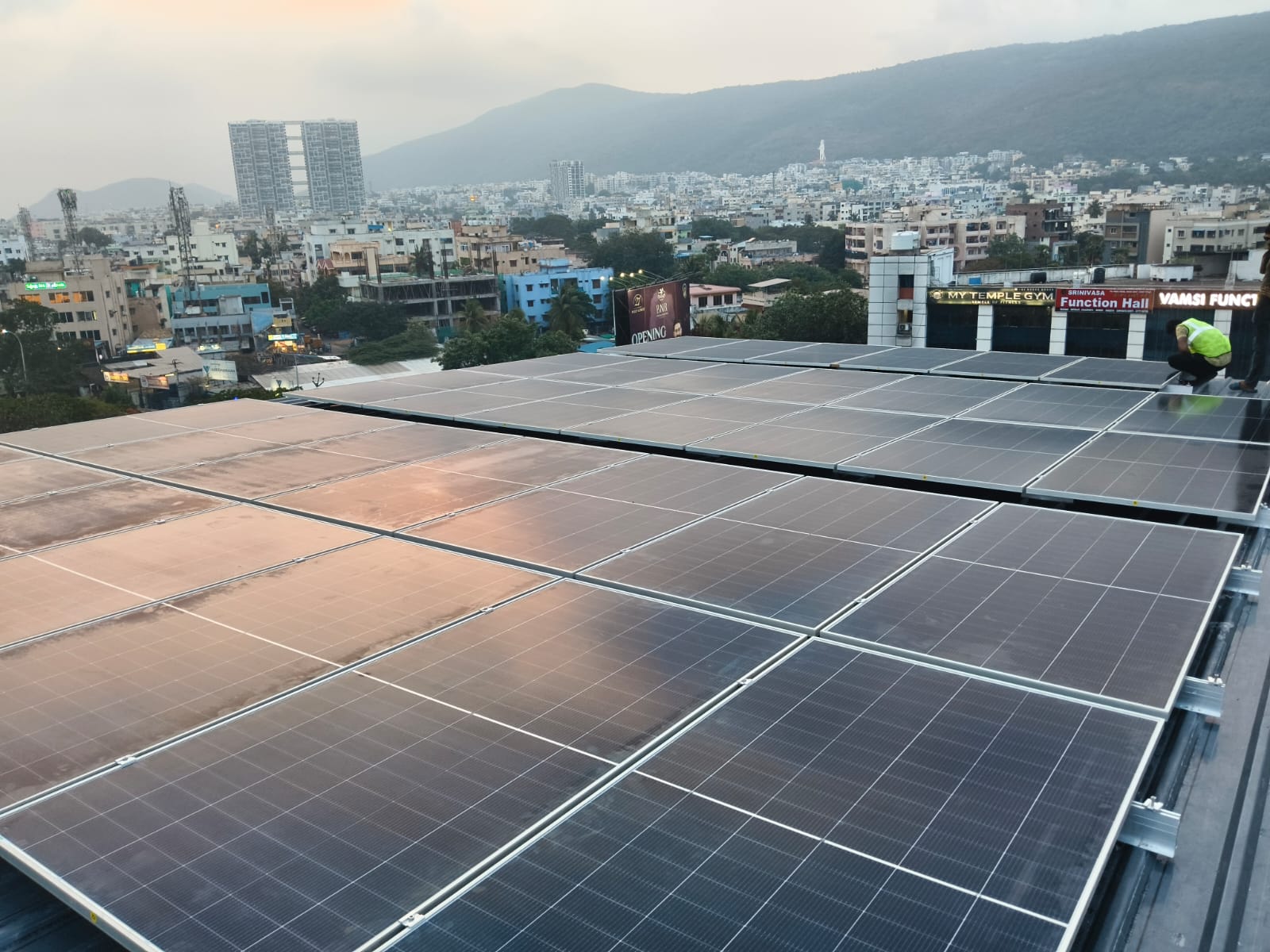 Rooftop solar panel installation overlooking Visakhapatnam city skyline at dusk