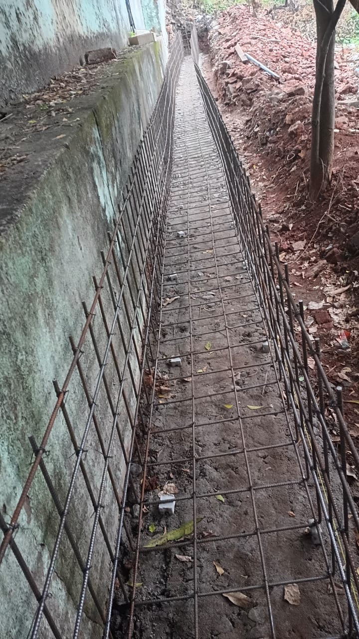 Steel reinforcement mesh laid inside an excavated trench along a boundary wall, ready for concreting